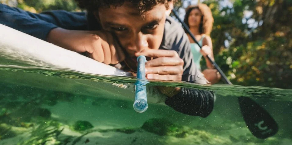A paddler drinks through a LifeStraw Sip Essential beside a kayak