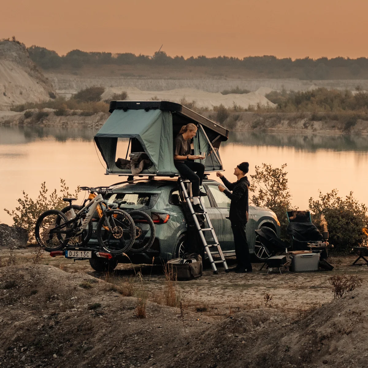 Thule Widesky rooftop tent open above a parked car beside two people and bicycles